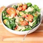 Hearty Plant-Based Salad with Balsamic Tahini Dressing recipe with carrots, brussel sprouts, cauliflower florets, quinoa, and sun-dried tomatoes, sitting on a cutting board with a fork in it.